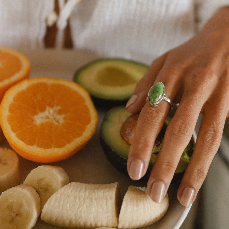 Woman’s hand wearing Green Turquoise Ring with oranges avocados and bananas in the background - womens turquoise jewellery by indie and harper