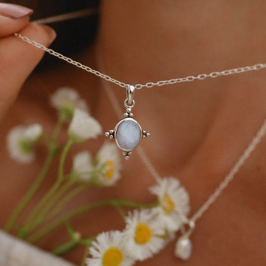 Woman holding up a sterling silver necklace with a rainbow moonstone in the middle and four points design