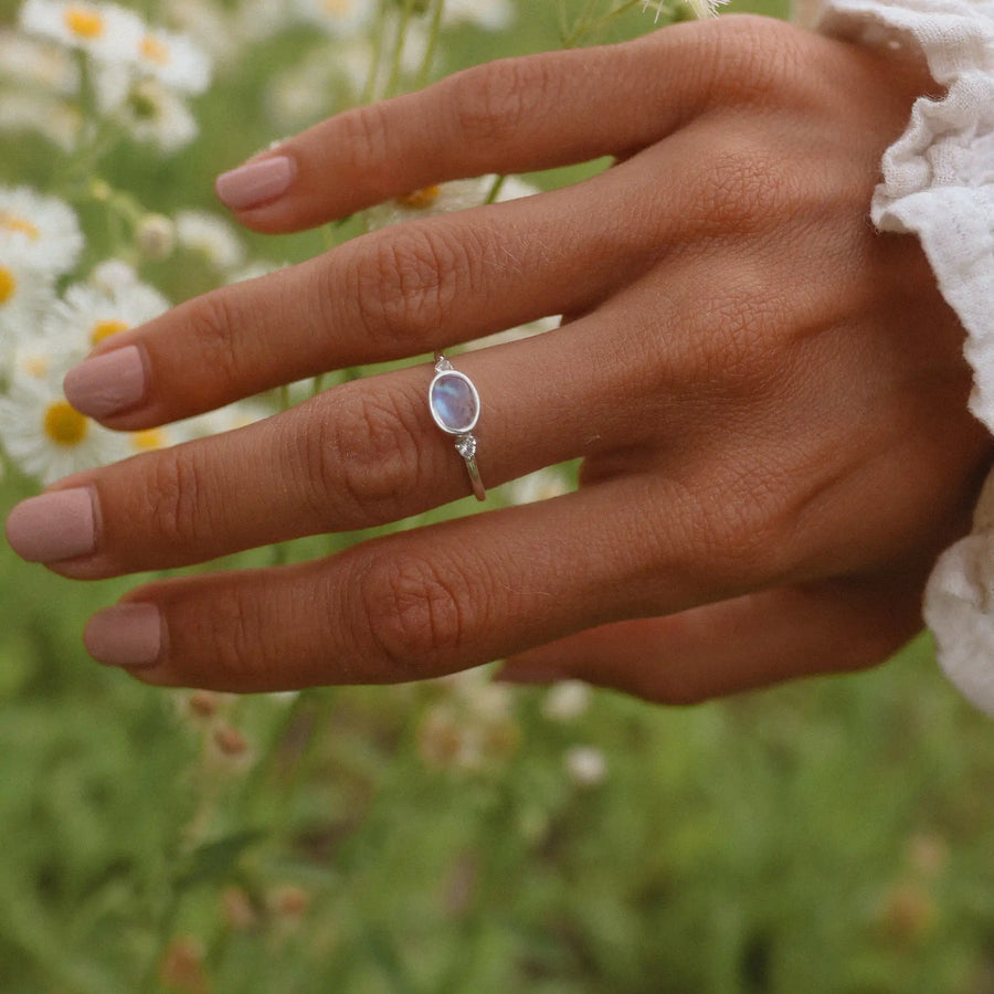 Woman's hand above a field of flowers, wearing a small topaz and moonstone ring - moonstone jewellery 
