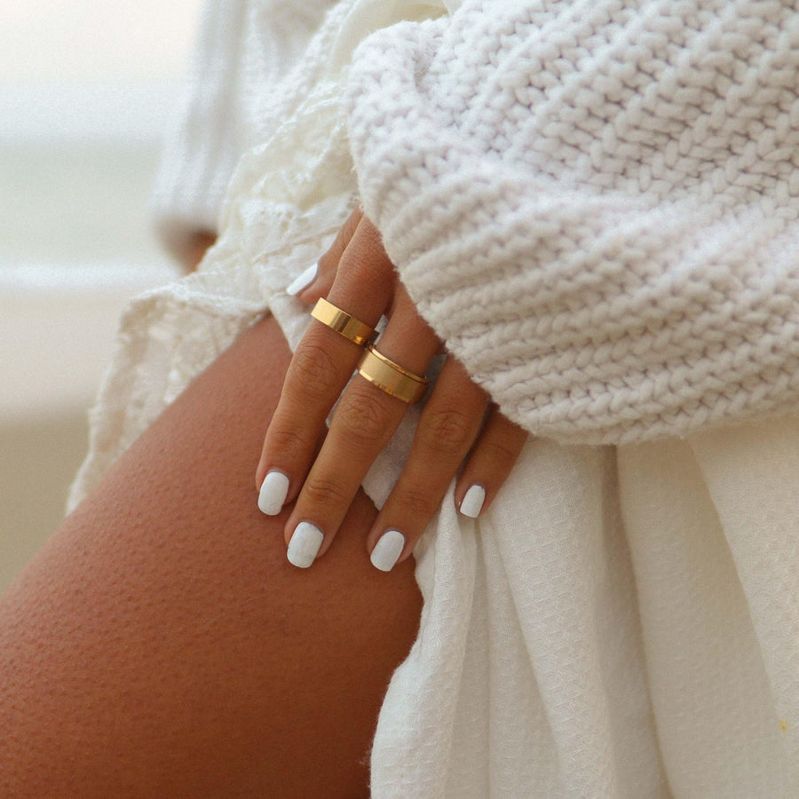 Woman wearing white and standing on a beach wearing gold rings - gold waterproof jewellery australia
