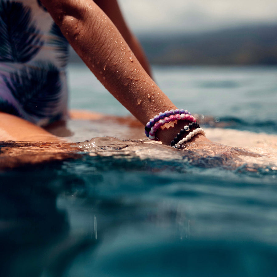 Person on surf board wearing Lokai waterproof Bracelets - womens waterproof jewellery - Australian jewellery online