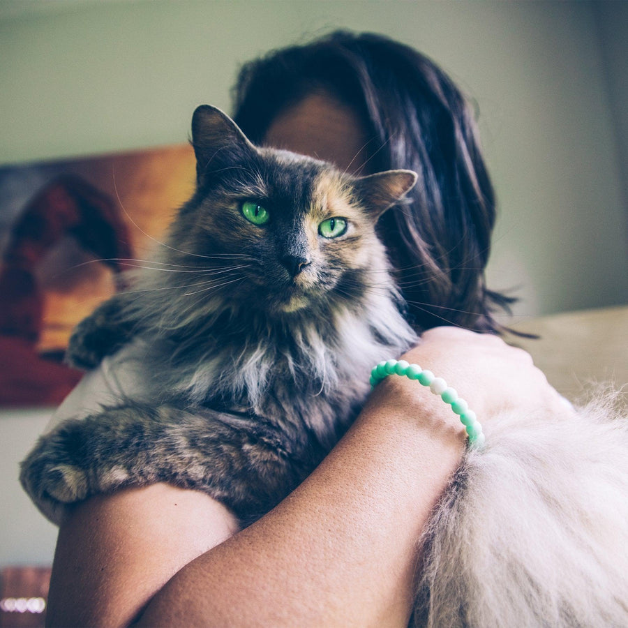 Woman cuddling a cat wearing green Lokai bracelet - meaningful jewellery - Australian jewellery brand