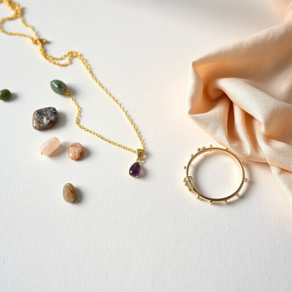 Delicate gold necklace, gemstone earrings, and bracelet arranged on a neutral linen surface with scattered stones