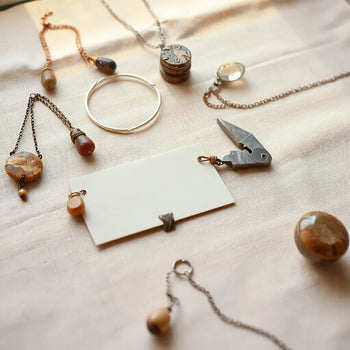 Delicate handcrafted necklaces and bracelets with natural stones arranged on linen under warm light.