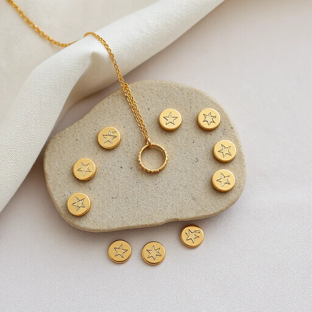 Delicate zodiac charm necklace and rings arranged on a neutral stone surface with constellation motifs