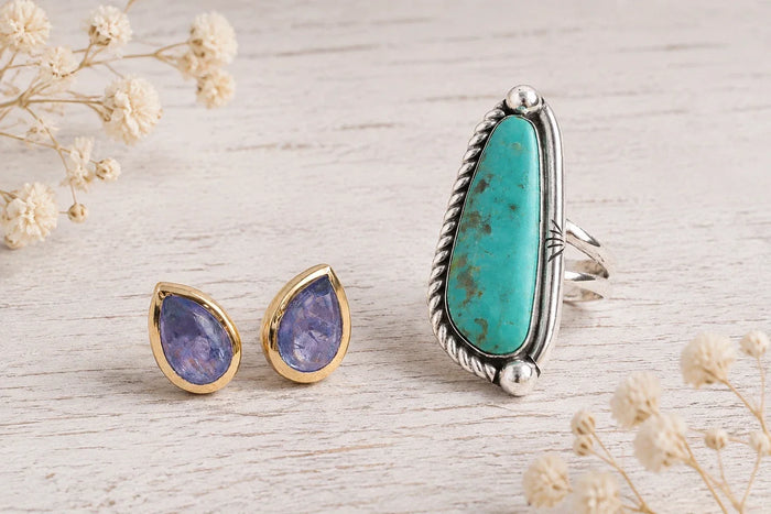 gold tanzanite stud earrings beside blue turquoise ring on a neutral background