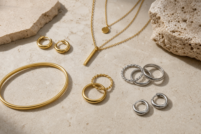 Waterproof hoop earrings, stacker rings, layered necklace, and bangle arranged on a neutral surface.