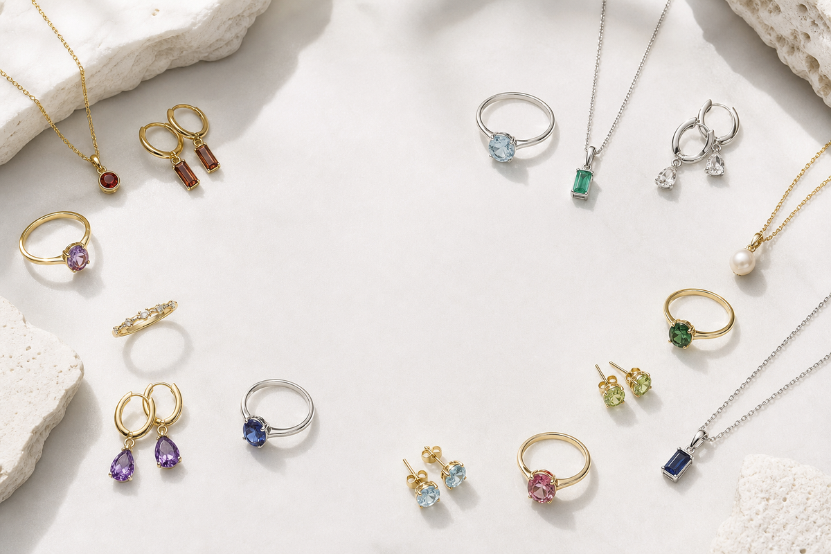 Editorial flat lay of assorted birthstone jewellery arranged on a pale stone surface.