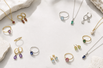 Editorial flat lay of assorted birthstone jewellery arranged on a pale stone surface.