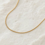 Gold chain necklace on a textured white surface
