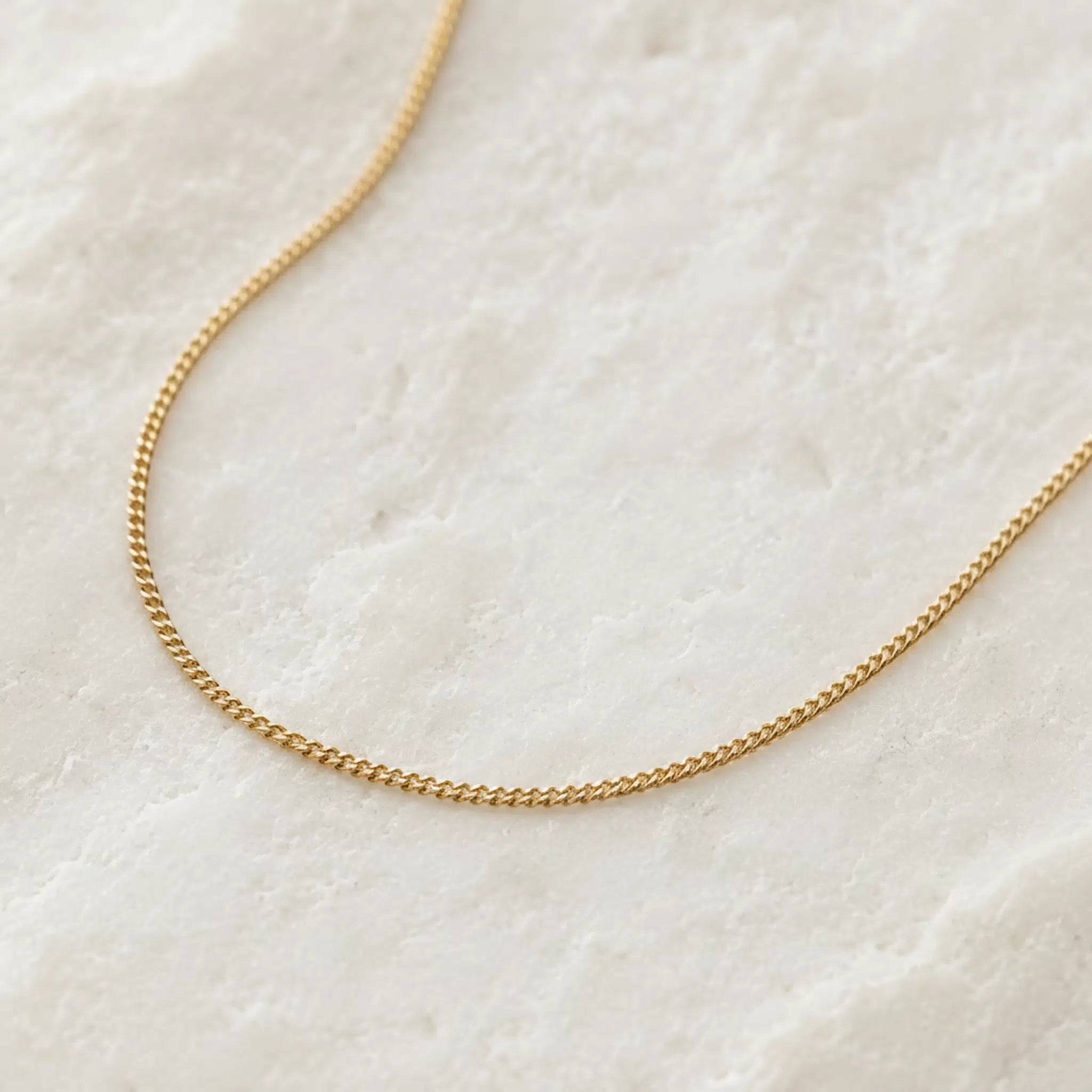 Gold chain necklace on a textured white surface