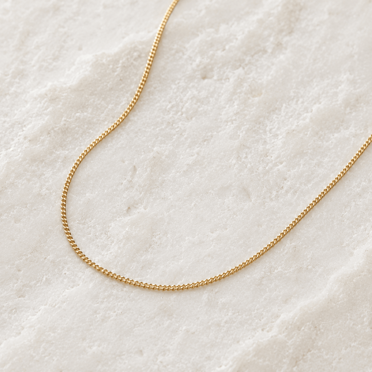 Gold chain necklace on a textured white surface