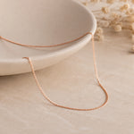18k Rose Gold Curb Chain Necklace laying on a light stone surface
