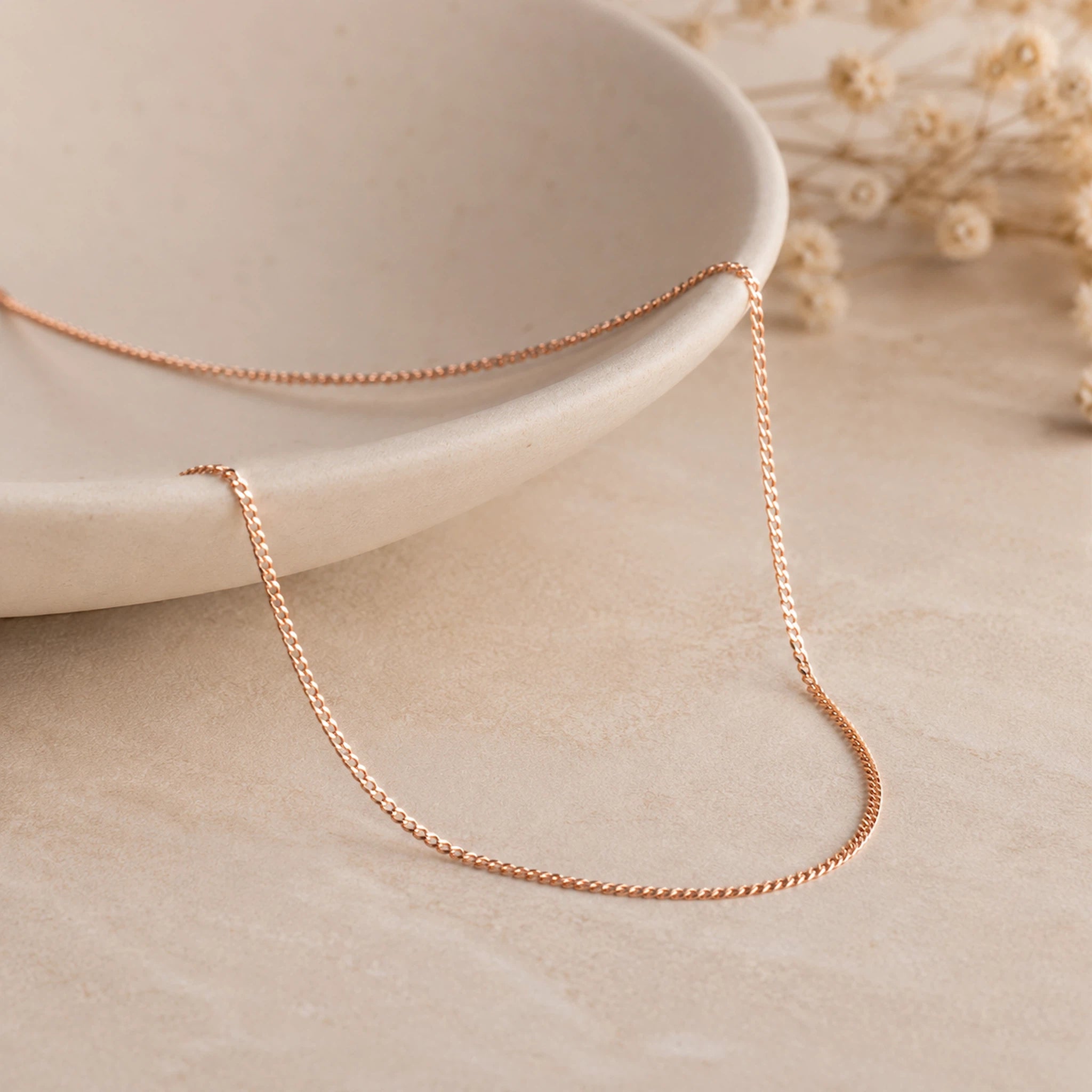 18k Rose Gold Curb Chain Necklace laying on a light stone surface