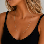 Close-up of a woman wearing a delicate  24 inch cable chain sterling silver necklace against a neutral background