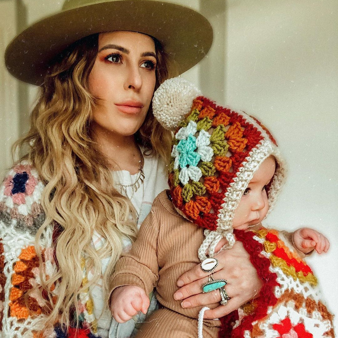 Woman holding a baby wearing a colorful crochet hat indoors