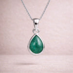 Sterling silver necklace with a green teardrop natural emerald gemstone pendant on a light pink background
