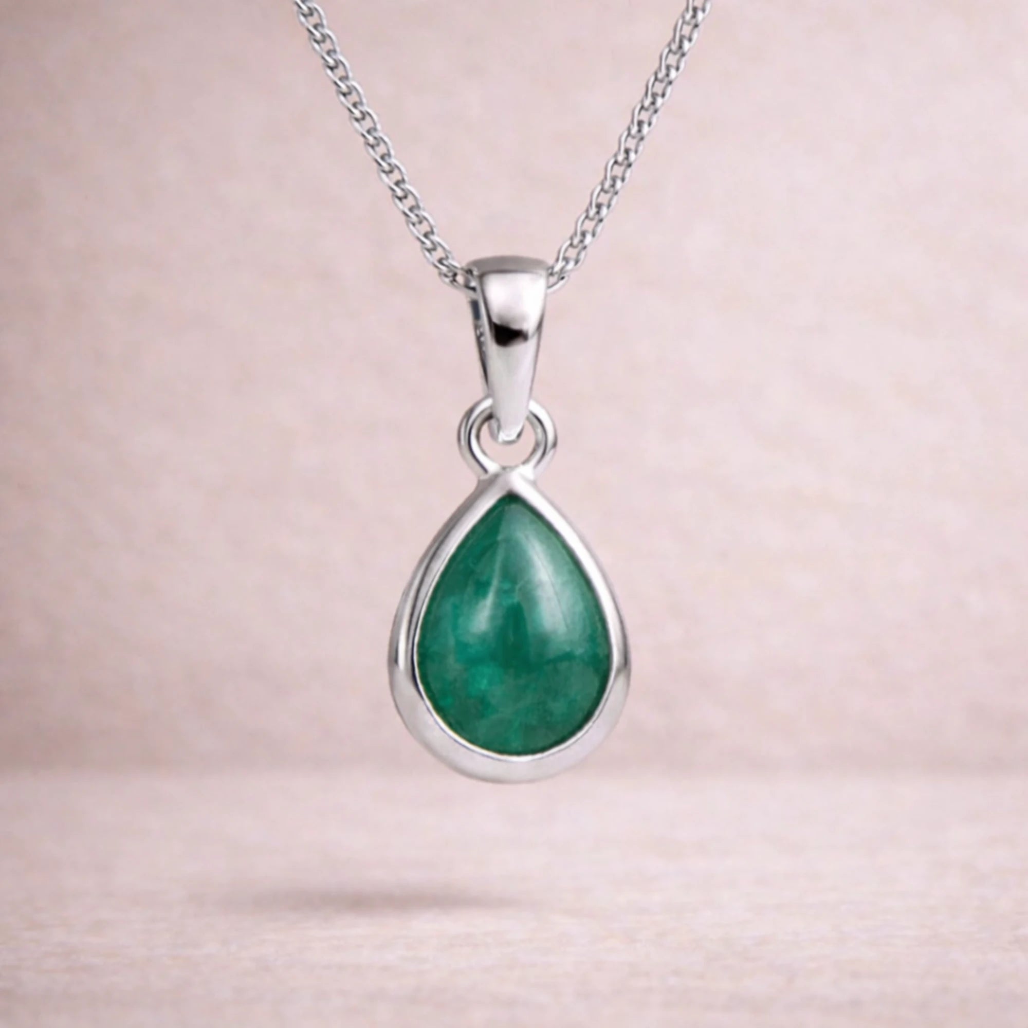 Sterling silver necklace with a green teardrop natural emerald gemstone pendant on a light pink background