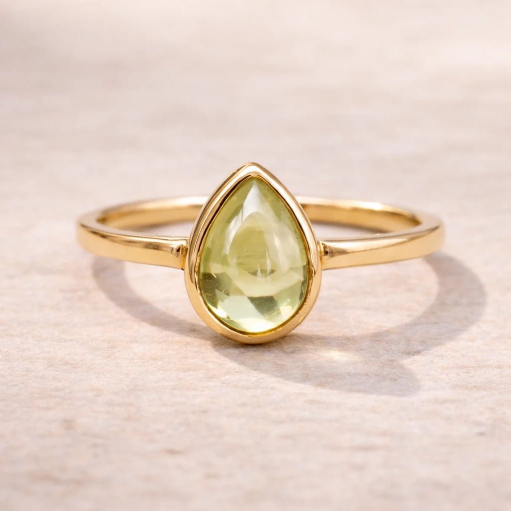 Gold ring with a teardrop-shaped green natural peridot gemstone on a light wooden background