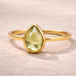 Gold ring with a green natural peridot gemstone on a light wooden surface