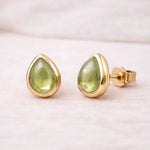 Gold stud earrings with green natural peridot gemstones on a light pink background