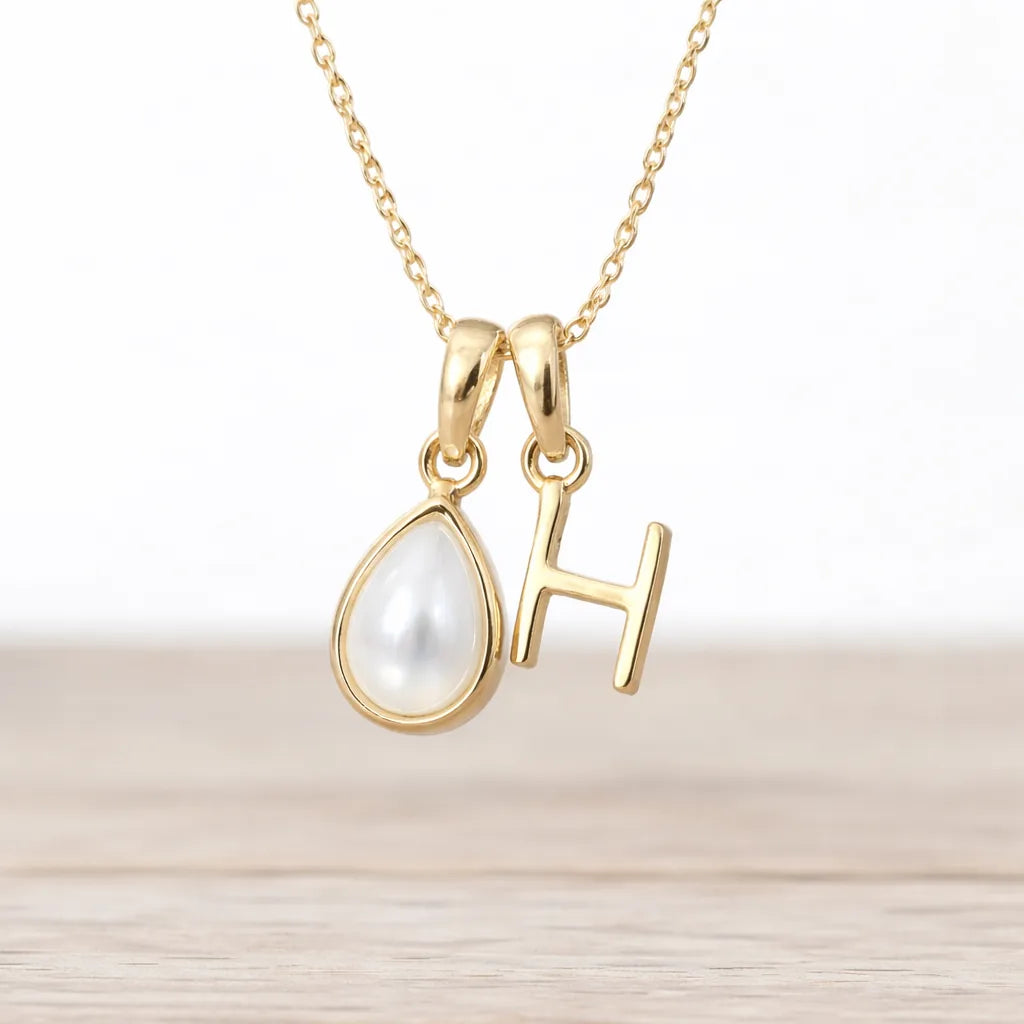 Gold necklace with a teardrop-shaped pendant and 'H' letter on a light background