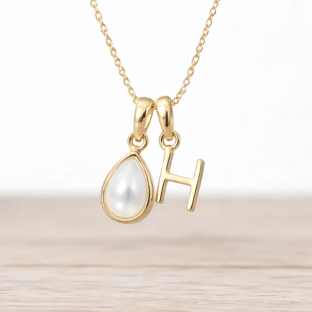 Gold necklace with a teardrop-shaped pendant and 'H' letter on a light background