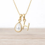 Gold necklace with a teardrop-shaped pendant and 'H' letter on a light background