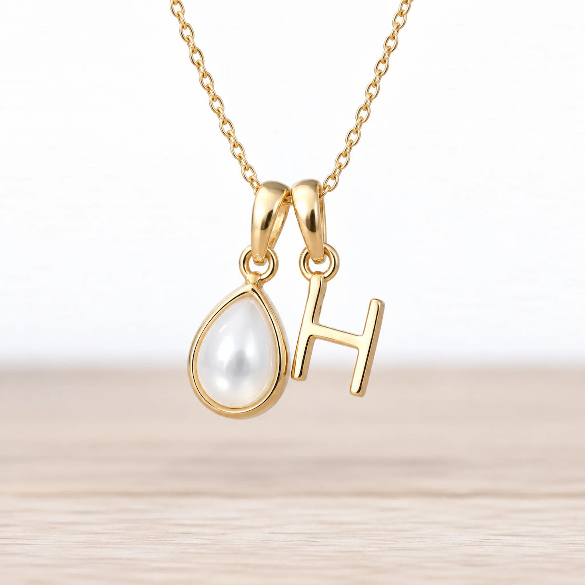 Gold June birthstone necklace with a pear-shaped natural mother of pearl pendant and letter 'H' charm.