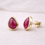 Gold stud earrings with natural ruby gemstones on a light background