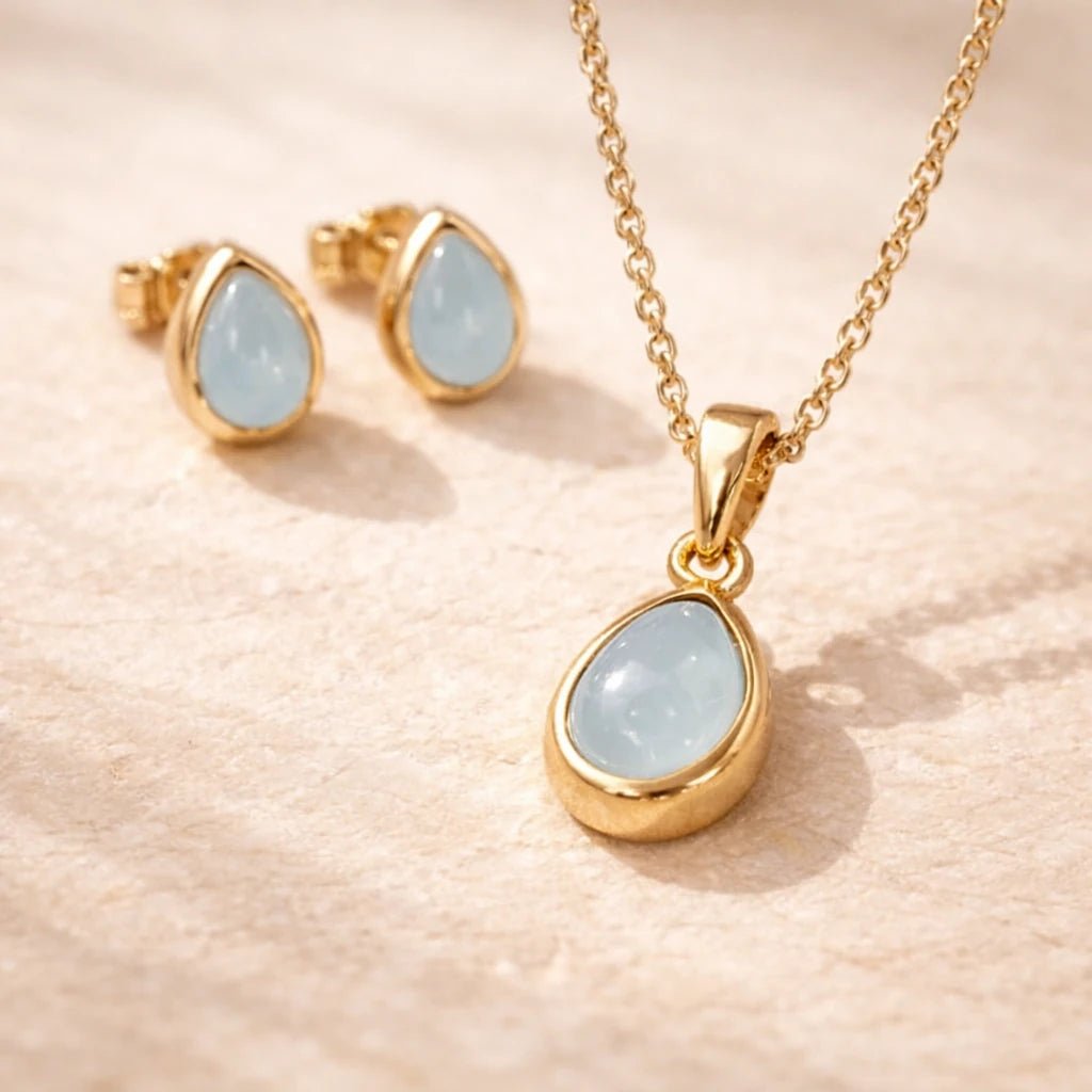Gold jewelry set with teardrop-shaped gemstones on a beige background