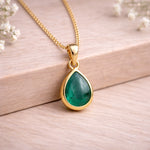 Gold necklace with a green teardrop natural emerald gemstone pendant on a wooden background