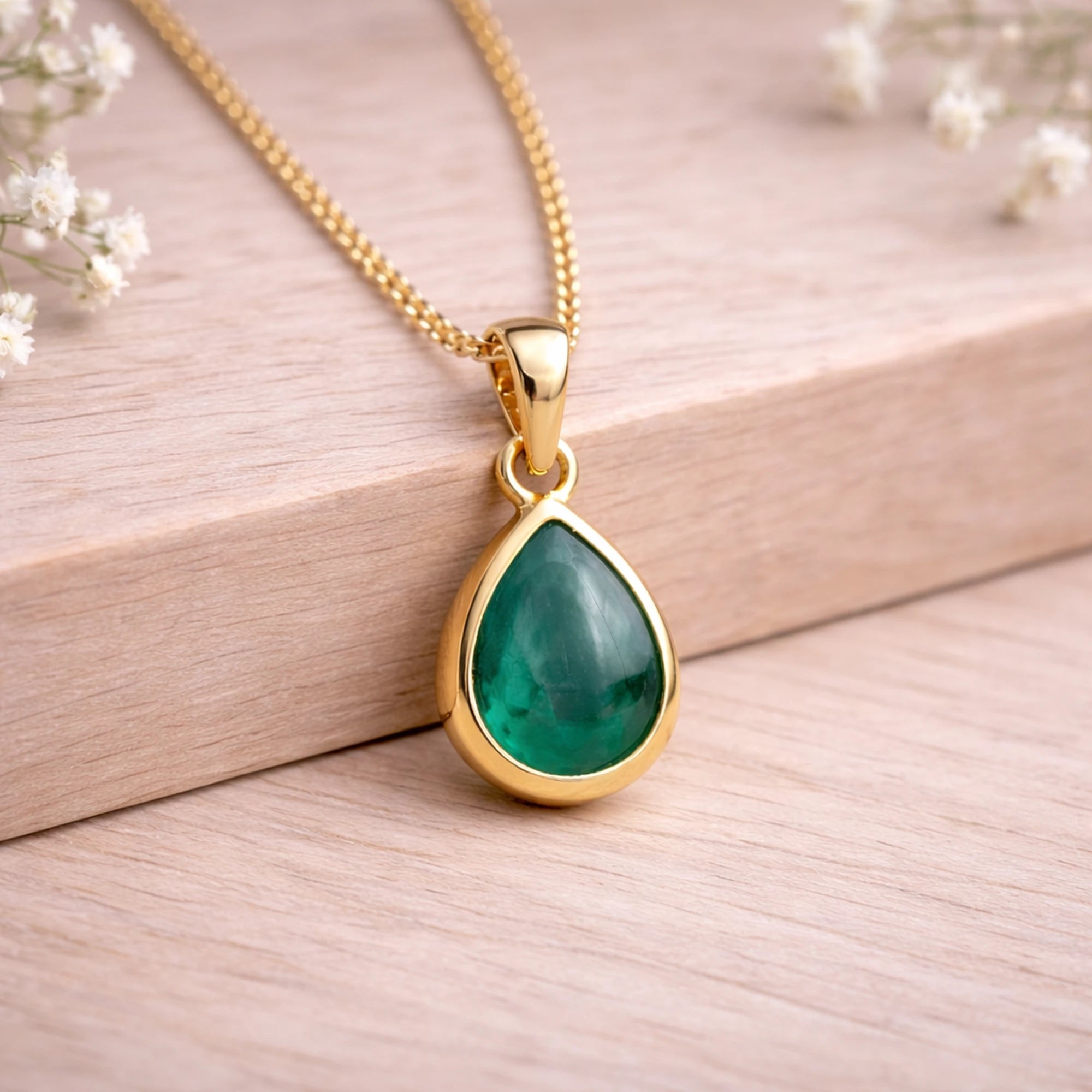 Gold necklace with a green teardrop natural emerald gemstone pendant on a wooden background