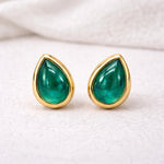 Gold stud earrings with green natural emerald teardrop stones on a light background