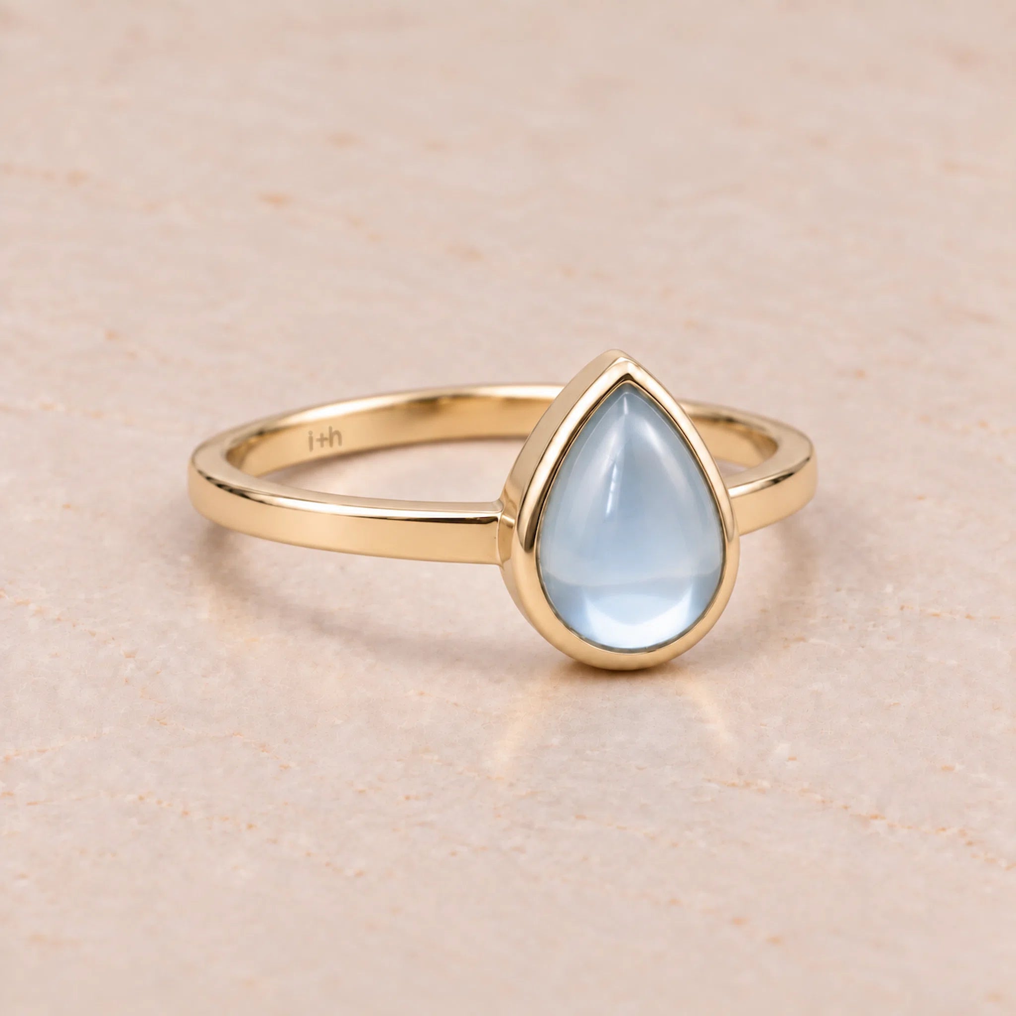 Gold November birthstone ring with a teardrop-shaped light blue natural topaz gemstone on a soft pink background