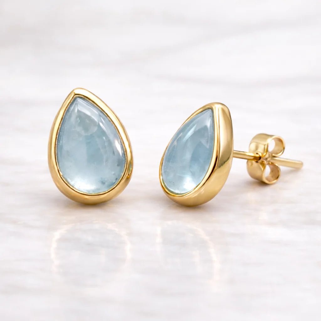 Gold earrings with teardrop-shaped light blue aquamarine gemstones on a white background