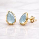 Gold earrings with teardrop-shaped light blue aquamarine gemstones on a white background