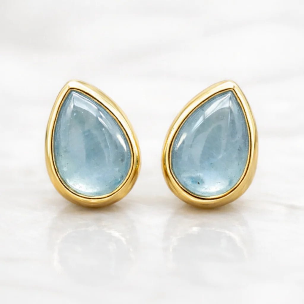 Gold-framed teardrop aquamarine stud earrings on a white background