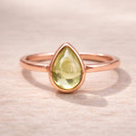 Rose gold ring with a green teardrop-shaped natural peridot gemstone on a beige background