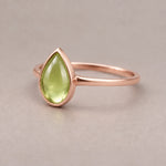 Rose gold August Birthstone ring with a pear-shaped cabochon bezel-set natural green peridot gemstone on a light background