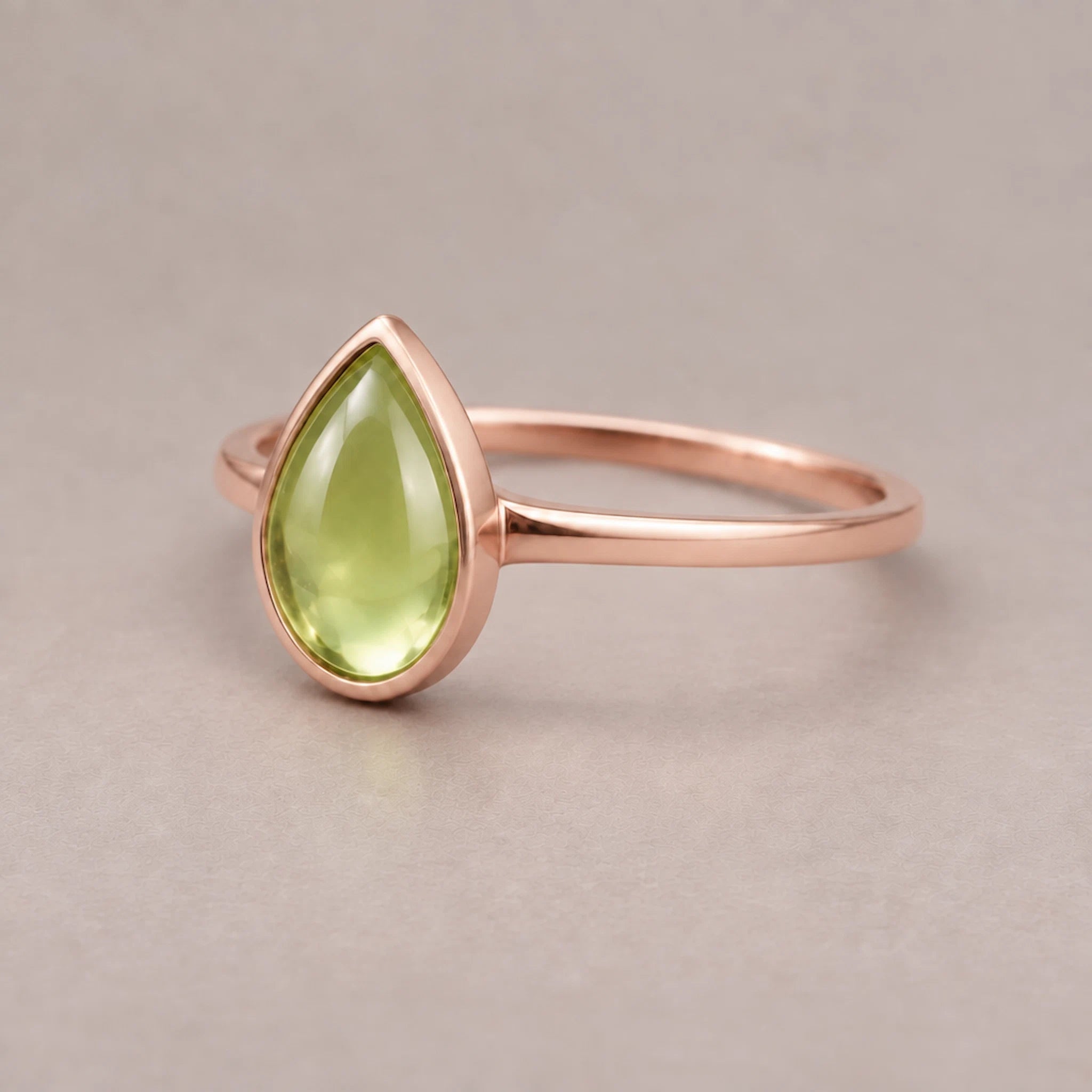 Rose gold August Birthstone ring with a pear-shaped cabochon bezel-set natural green peridot gemstone on a light background