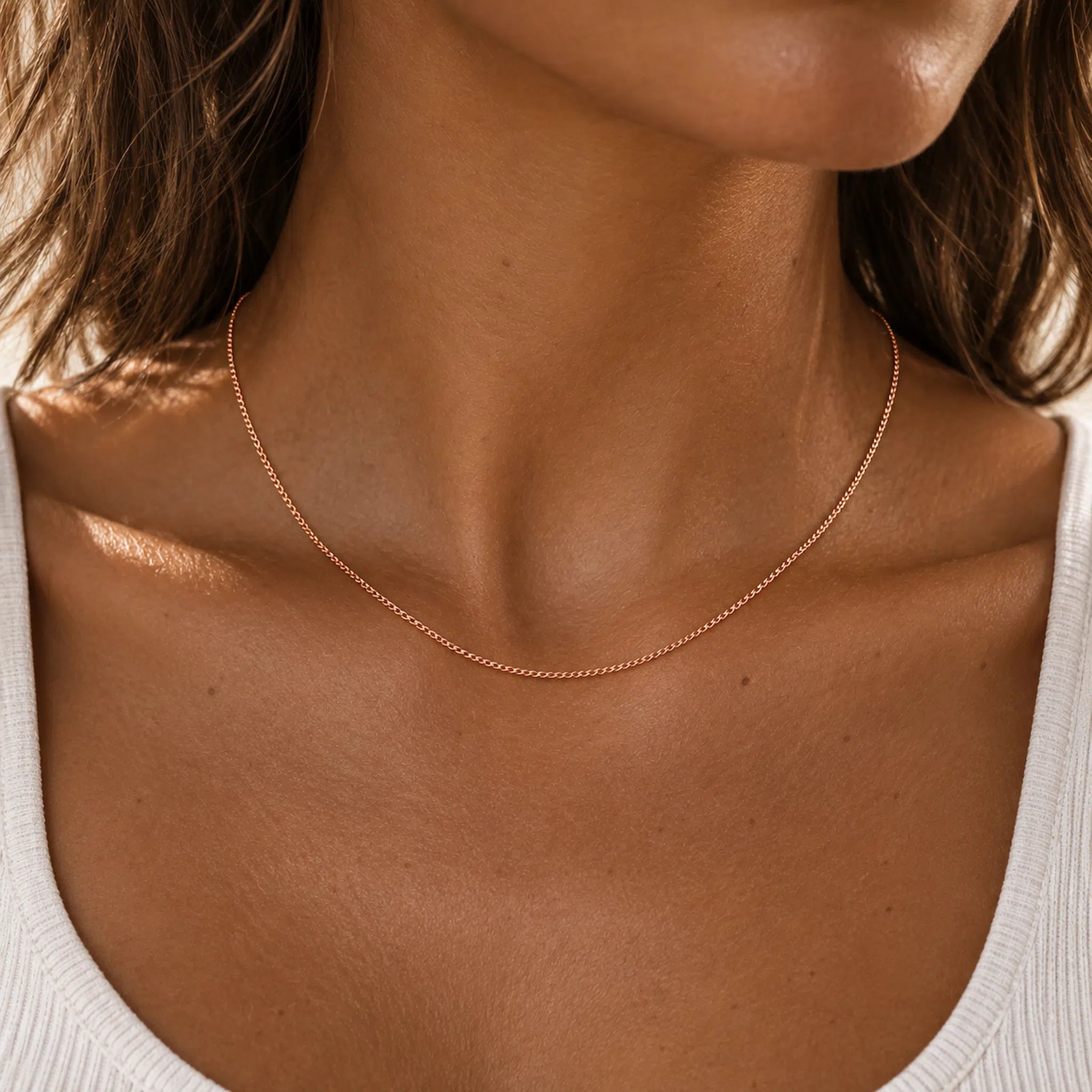 close up of a woman wearing a dainty minimalist 9k rose gold chain necklace with 1mm curb chain design and 16 inch length