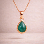 Rose Gold necklace with a green teardrop natural emerald gemstone pendant on a light pink background