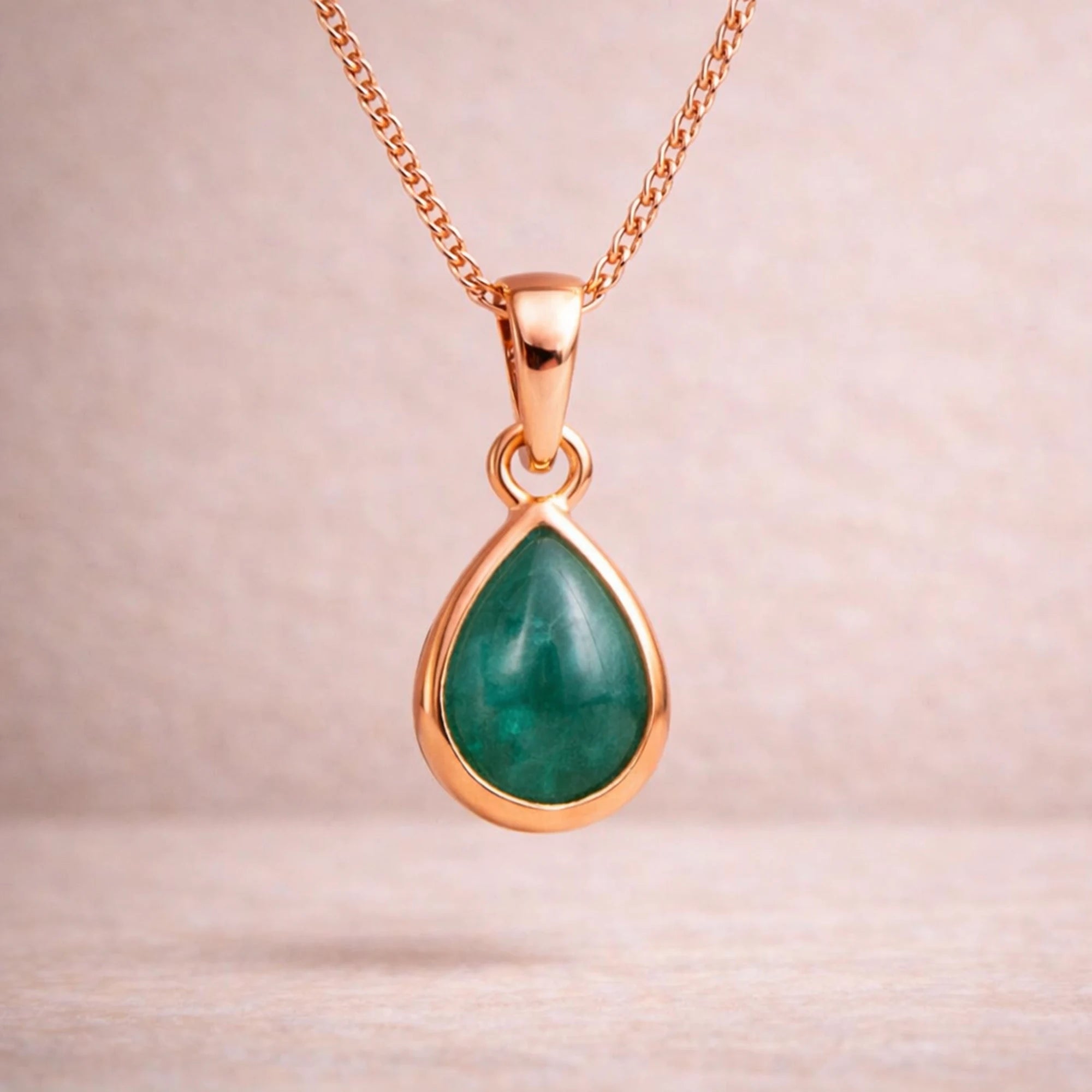 Rose Gold necklace with a green teardrop natural emerald gemstone pendant on a light pink background