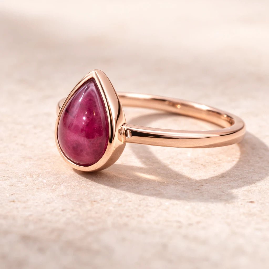Rose gold ring with a tear drop shaped natural ruby gemstone on a beige background