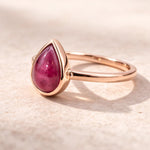 Rose gold ring with a tear drop shaped natural ruby gemstone on a beige background