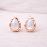 Teardrop-shaped natural pearl earrings with rose gold frames on a light pink background