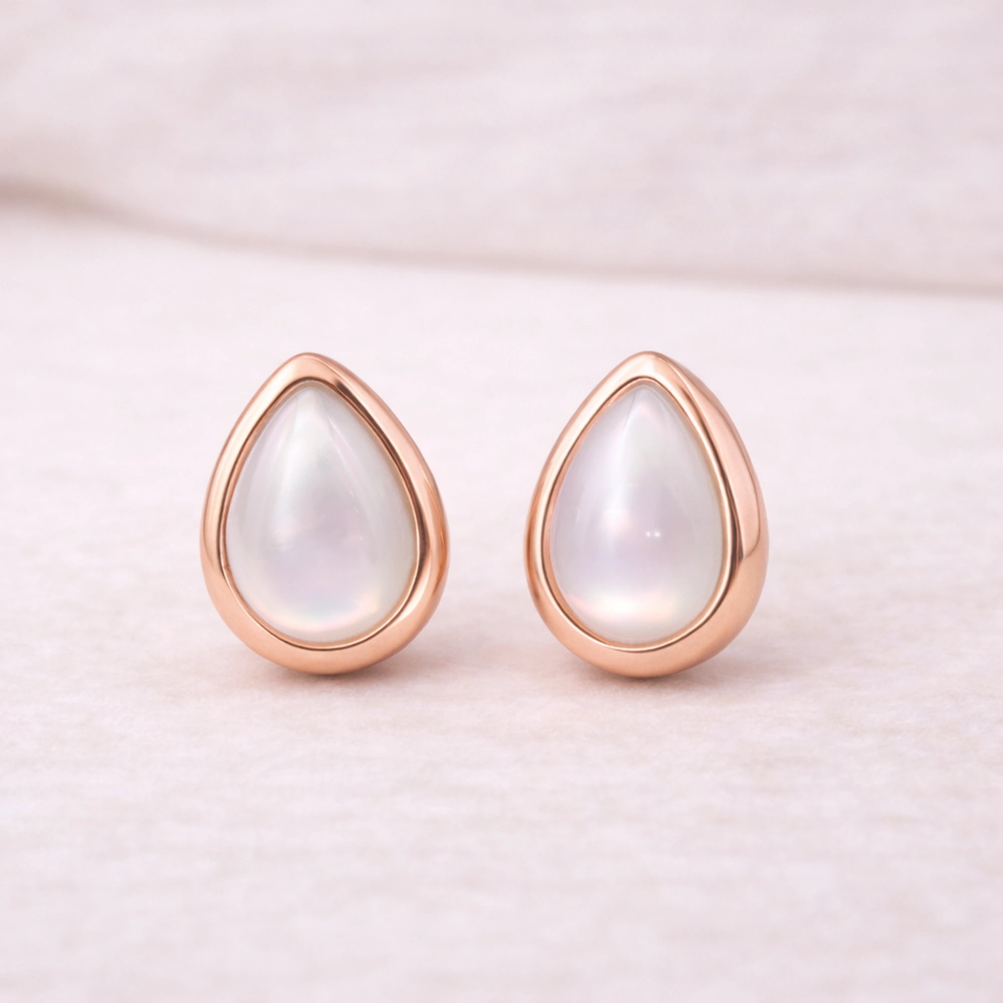 Teardrop-shaped natural pearl earrings with rose gold frames on a light pink background