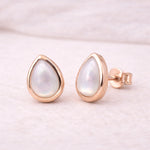 Rose gold earrings with teardrop-shaped white pearls on a light pink background