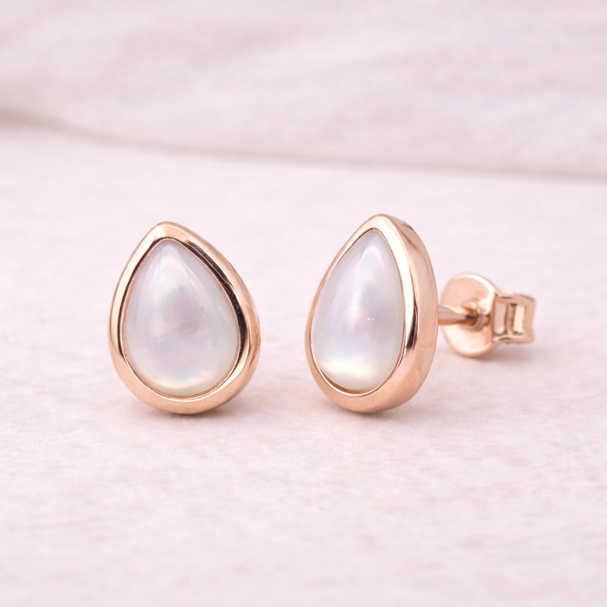 Rose gold earrings with teardrop-shaped white pearls on a light pink background